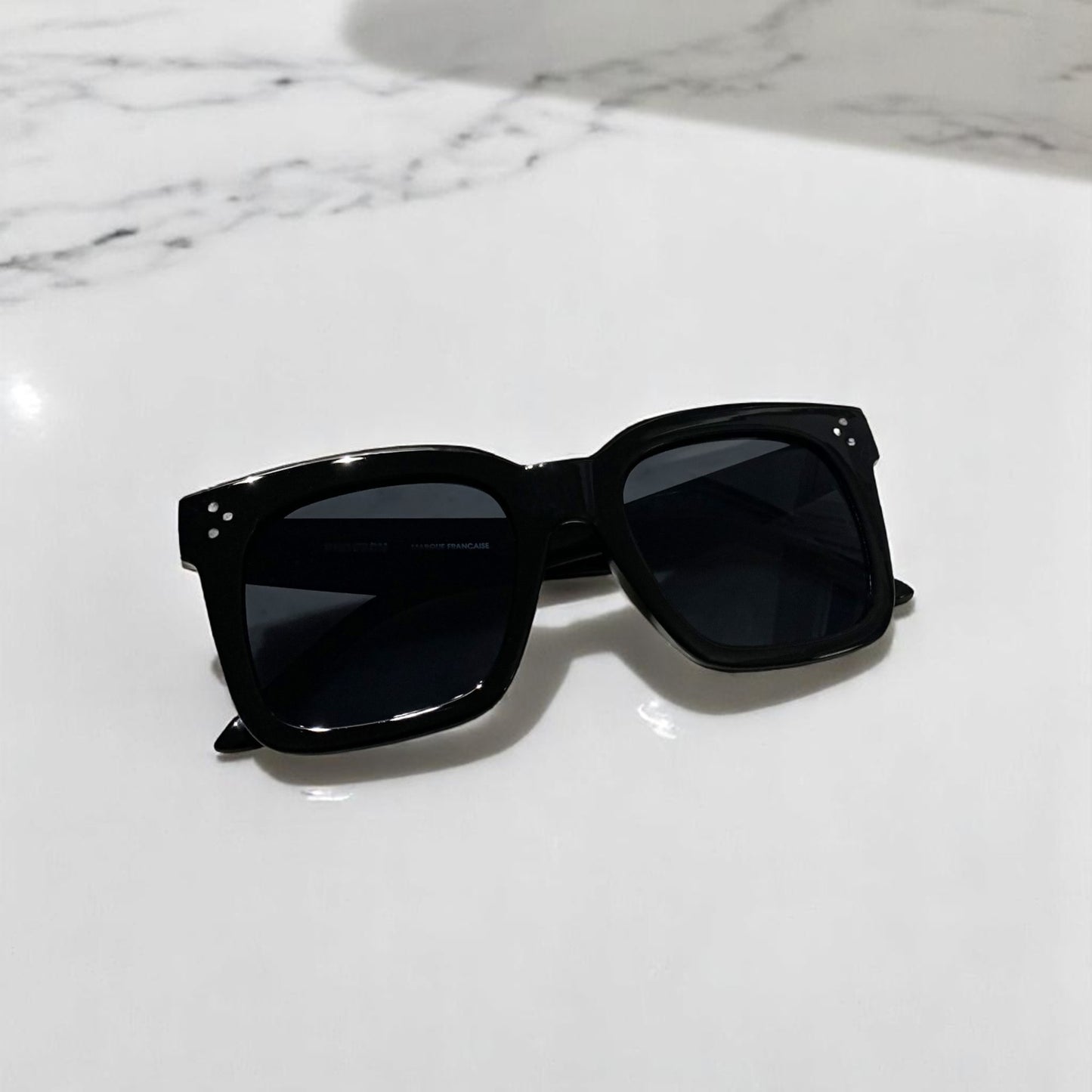Lunettes de soleil Pinigoon oversize noir fermées sur comptoir en marbre
