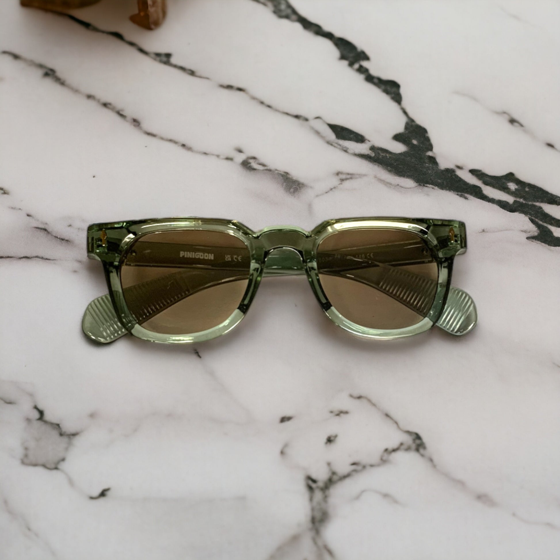 Lunettes de soleil PINIGOON la numéro 8 gris vert posée sur support en marbre